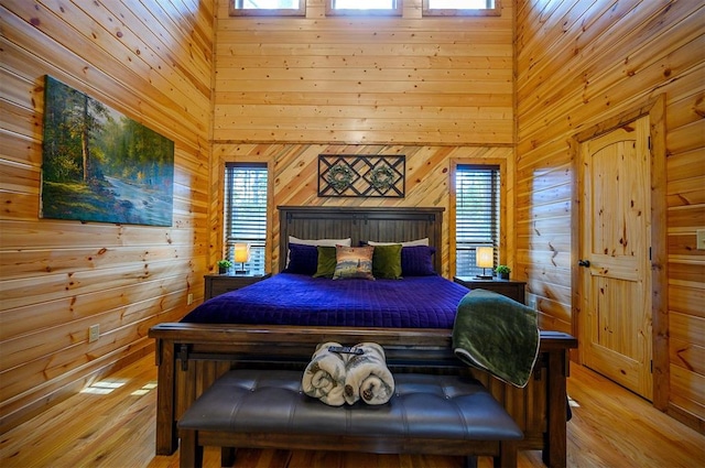 bedroom featuring wooden walls, light hardwood / wood-style flooring, and a high ceiling