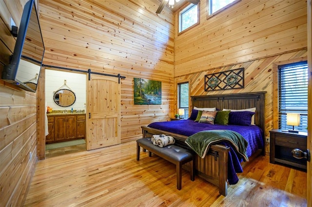 bedroom featuring connected bathroom, wood walls, a high ceiling, and light hardwood / wood-style flooring