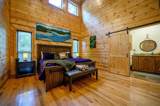 bedroom featuring high vaulted ceiling, a barn door, and wooden walls