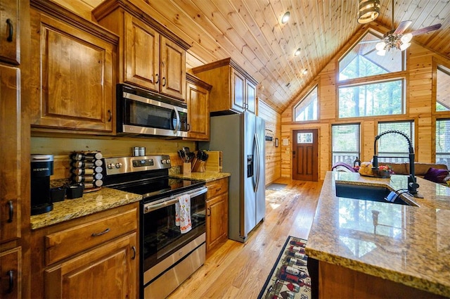 kitchen featuring appliances with stainless steel finishes, light wood-type flooring, light stone counters, sink, and wood walls