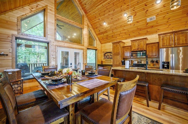 dining room with wood walls, french doors, high vaulted ceiling, and light wood-type flooring