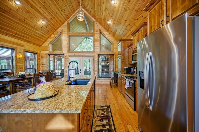 kitchen featuring stainless steel appliances, a kitchen island with sink, wooden walls, sink, and light hardwood / wood-style floors