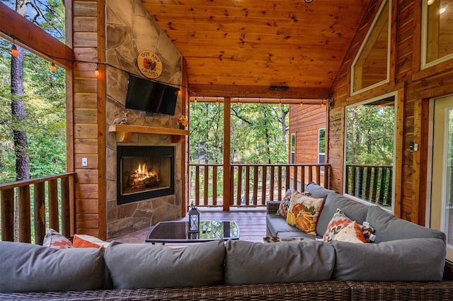 sunroom / solarium with an outdoor stone fireplace, wood ceiling, and vaulted ceiling