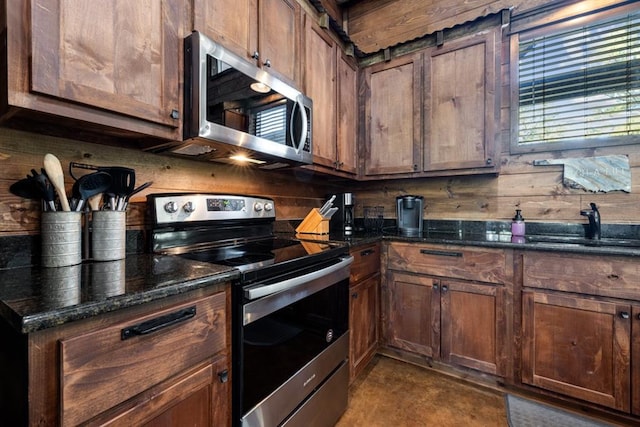 kitchen with wooden walls, dark stone countertops, sink, and appliances with stainless steel finishes