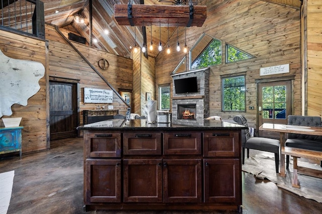 kitchen with dark brown cabinets, wood walls, a stone fireplace, and high vaulted ceiling