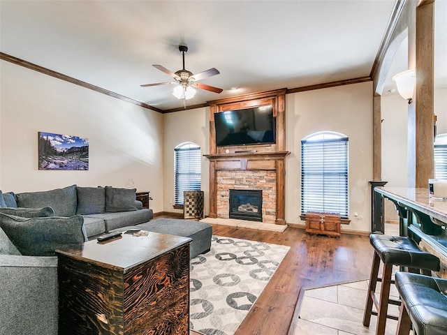 living room featuring ceiling fan, a stone fireplace, light wood-type flooring, and ornamental molding