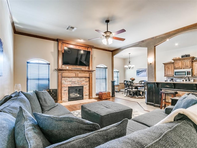 living room with ceiling fan with notable chandelier, crown molding, light wood-type flooring, and a fireplace