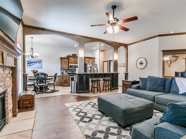 living room with a fireplace, crown molding, light hardwood / wood-style flooring, and ceiling fan with notable chandelier