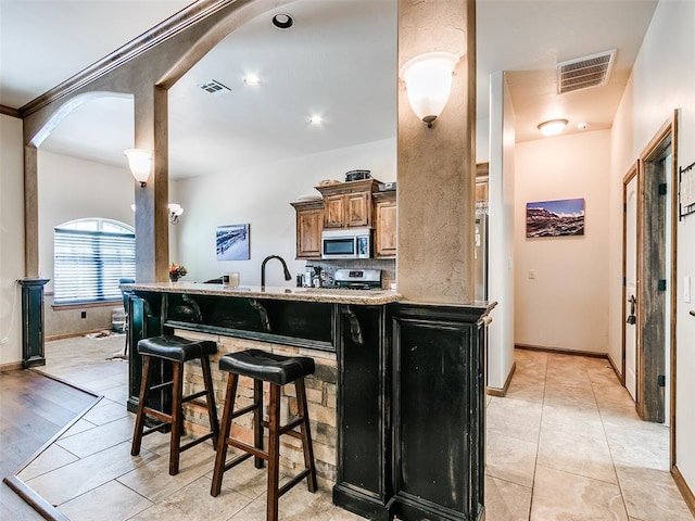 kitchen featuring a kitchen breakfast bar, light stone counters, light tile patterned floors, and stainless steel appliances