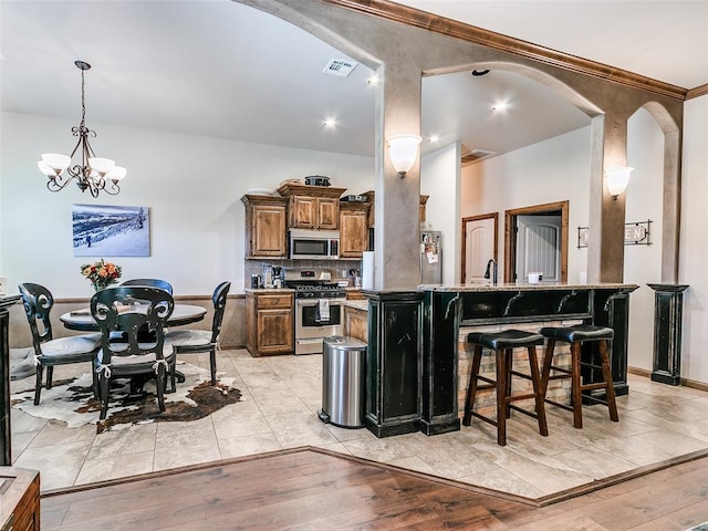 kitchen featuring kitchen peninsula, appliances with stainless steel finishes, light wood-type flooring, a kitchen breakfast bar, and a chandelier