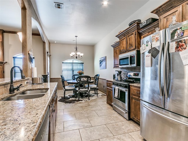 kitchen with sink, hanging light fixtures, a notable chandelier, light stone counters, and stainless steel appliances