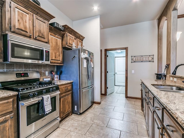 kitchen with sink, light tile patterned floors, appliances with stainless steel finishes, tasteful backsplash, and light stone counters