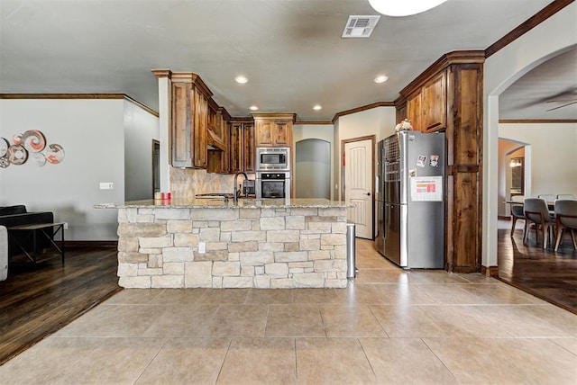 kitchen featuring kitchen peninsula, a kitchen breakfast bar, light stone countertops, stainless steel appliances, and light hardwood / wood-style floors