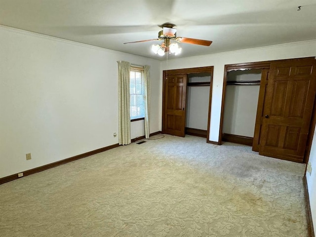 unfurnished bedroom featuring ceiling fan, crown molding, light colored carpet, and two closets