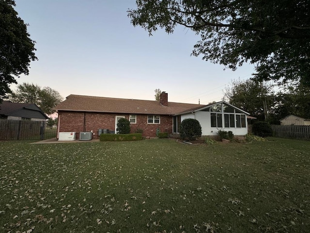 back house at dusk with a lawn, a sunroom, and central AC