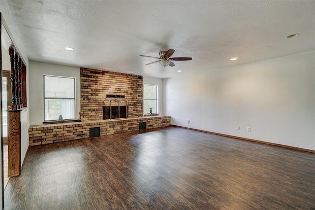 unfurnished living room with ceiling fan, dark hardwood / wood-style flooring, a textured ceiling, and a brick fireplace