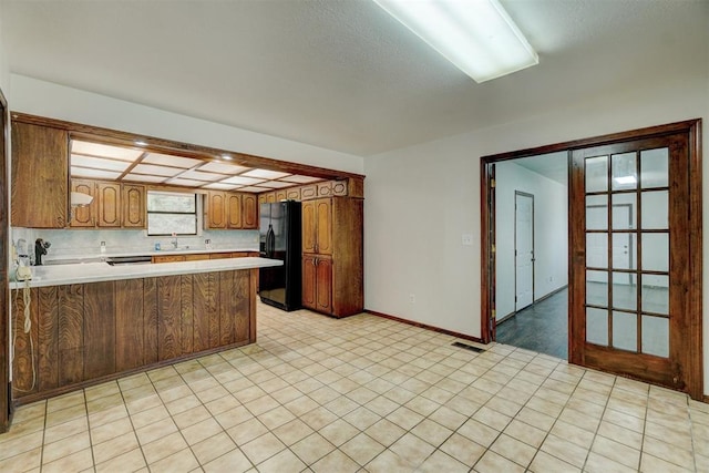 kitchen featuring kitchen peninsula, french doors, tasteful backsplash, black fridge with ice dispenser, and sink