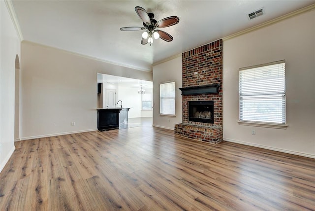 unfurnished living room featuring sink, crown molding, hardwood / wood-style flooring, ceiling fan, and a fireplace