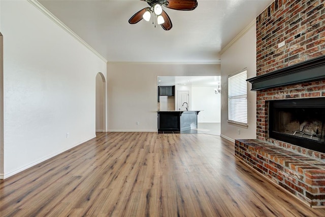 unfurnished living room with sink, a brick fireplace, hardwood / wood-style flooring, ceiling fan, and ornamental molding