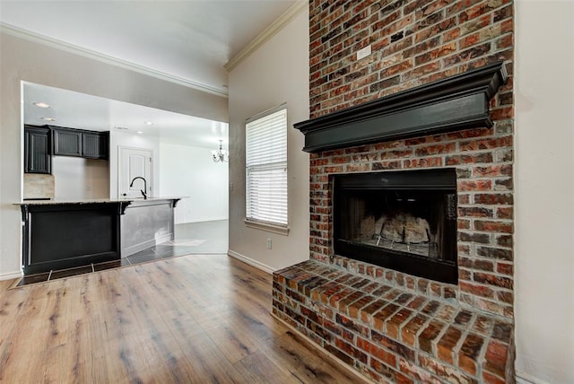 living room with sink, a brick fireplace, an inviting chandelier, dark hardwood / wood-style floors, and ornamental molding