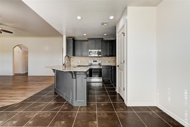 kitchen with appliances with stainless steel finishes, a kitchen breakfast bar, tasteful backsplash, light stone counters, and dark hardwood / wood-style floors