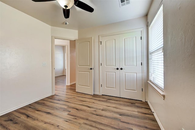 unfurnished bedroom featuring multiple windows, ceiling fan, a closet, and light hardwood / wood-style floors