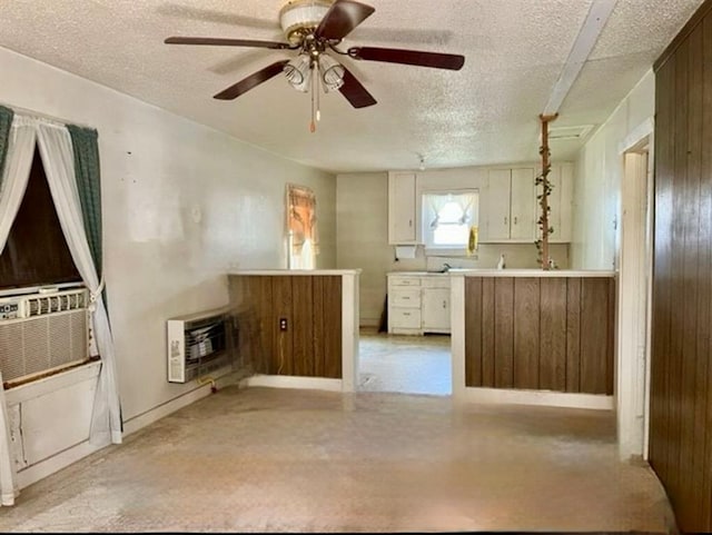 kitchen featuring a textured ceiling, heating unit, cooling unit, ceiling fan, and wooden walls