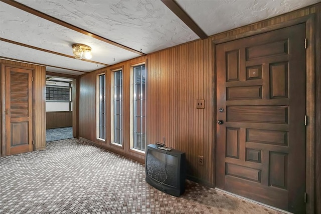 hallway featuring carpet, wood walls, and a textured ceiling