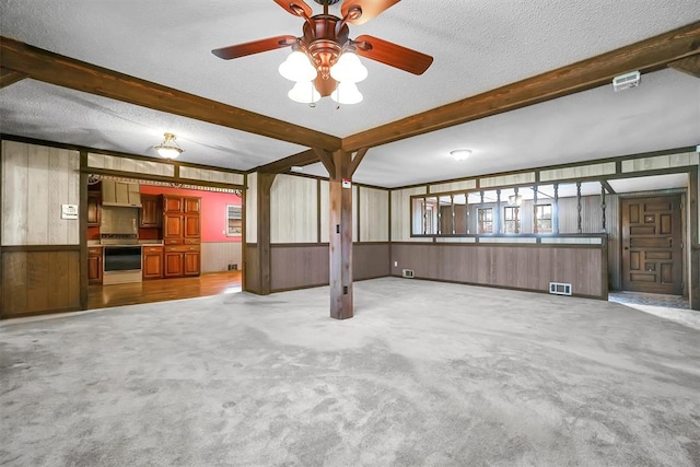 interior space with a textured ceiling, beam ceiling, visible vents, and wooden walls