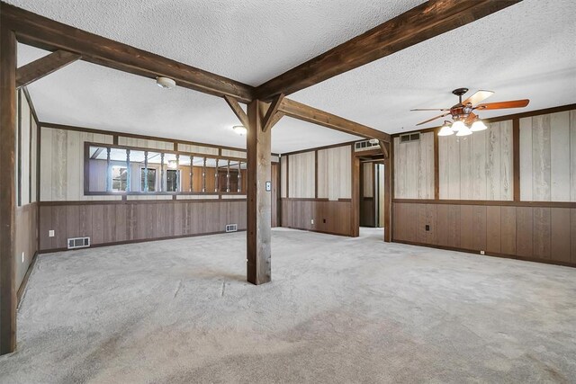 interior space with wooden walls, a textured ceiling, visible vents, and beam ceiling