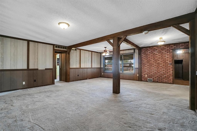 carpeted empty room featuring a textured ceiling, beam ceiling, visible vents, and wooden walls