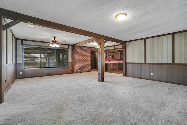 unfurnished room featuring a textured ceiling, beamed ceiling, carpet, and wooden walls