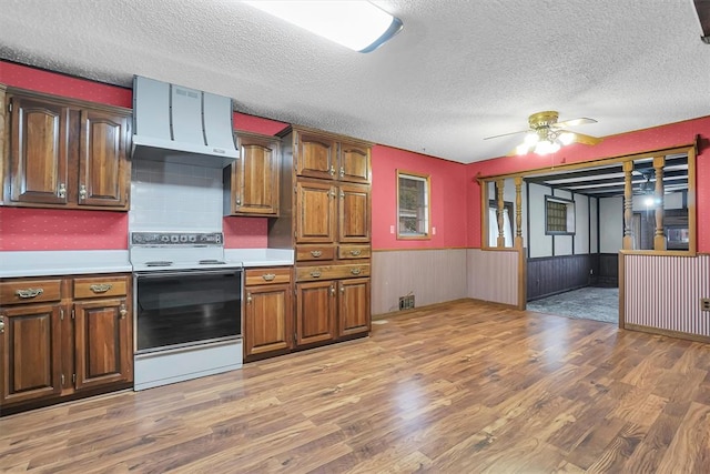 kitchen with a wainscoted wall, light wood finished floors, electric range oven, and light countertops