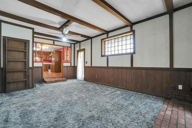 unfurnished living room with built in features, beam ceiling, wainscoting, a textured ceiling, and wooden walls