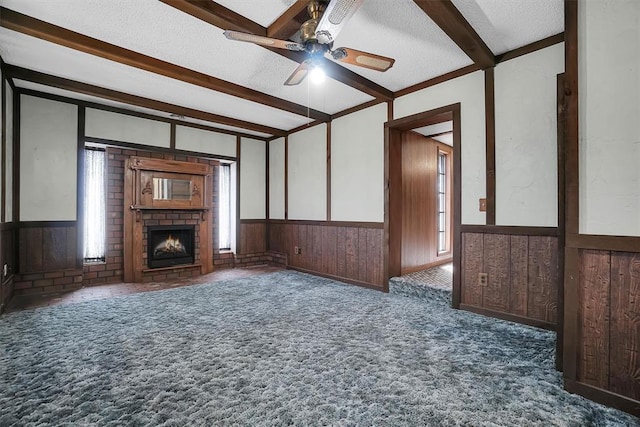 unfurnished living room featuring a wainscoted wall, a textured ceiling, a fireplace, and beamed ceiling