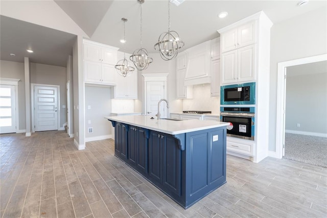 kitchen featuring appliances with stainless steel finishes, white cabinetry, a sink, blue cabinets, and premium range hood