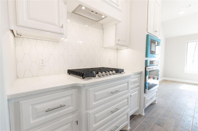 kitchen featuring custom exhaust hood, stainless steel appliances, decorative backsplash, white cabinetry, and baseboards