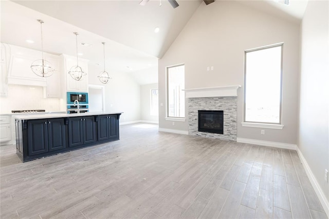 unfurnished living room featuring light wood-type flooring, a wealth of natural light, a glass covered fireplace, and high vaulted ceiling