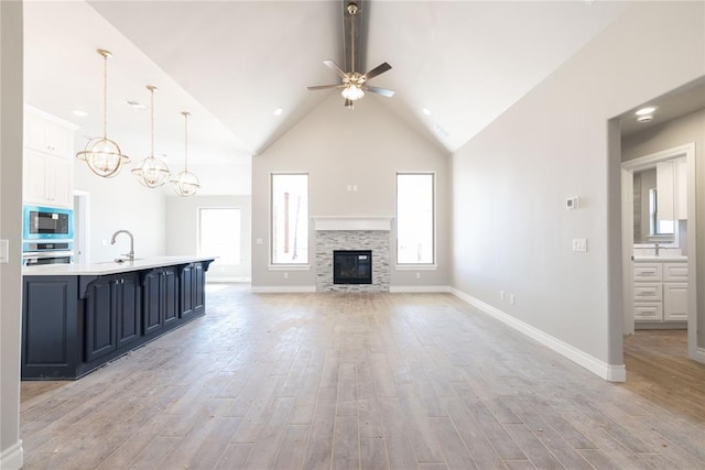 unfurnished living room featuring light wood-style flooring, high vaulted ceiling, baseboards, and ceiling fan with notable chandelier