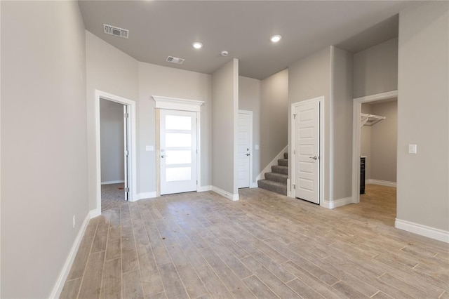 unfurnished room featuring light wood-type flooring, visible vents, stairway, and baseboards