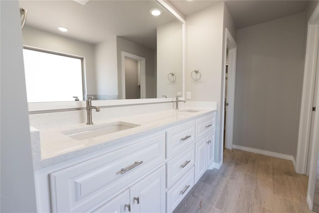 bathroom featuring double vanity, wood finished floors, a sink, and recessed lighting