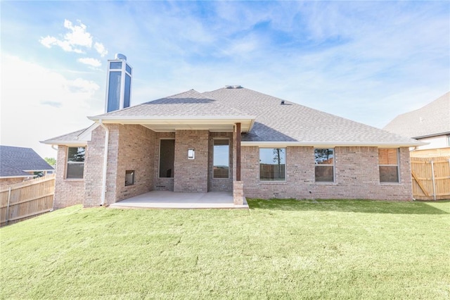 back of house featuring a patio area, a lawn, fence, brick siding, and roof with shingles