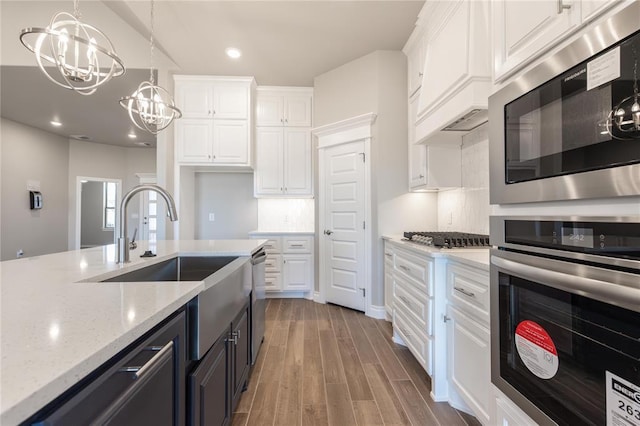 kitchen featuring stainless steel appliances, a sink, a notable chandelier, and white cabinetry