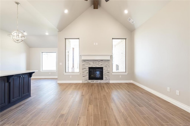 unfurnished living room featuring visible vents, light wood-type flooring, baseboards, a glass covered fireplace, and ceiling fan with notable chandelier