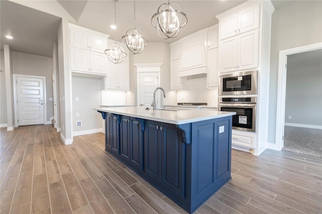kitchen featuring blue cabinets, stainless steel appliances, light wood finished floors, a sink, and a chandelier