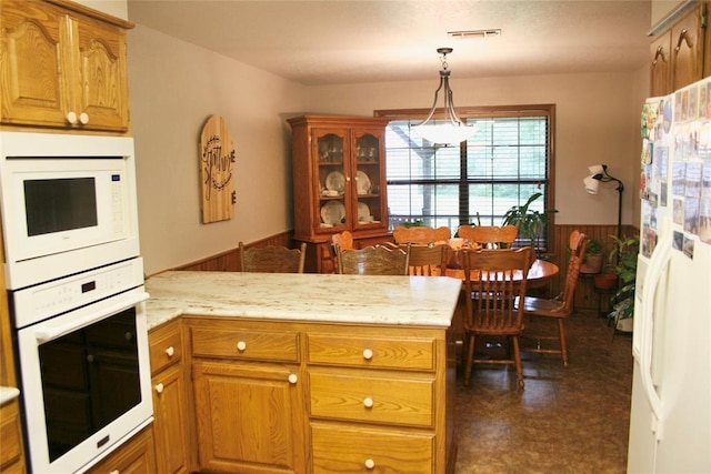 kitchen with kitchen peninsula, white appliances, decorative light fixtures, and wooden walls