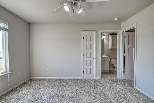 unfurnished bedroom with multiple windows, ceiling fan, ensuite bathroom, and light colored carpet