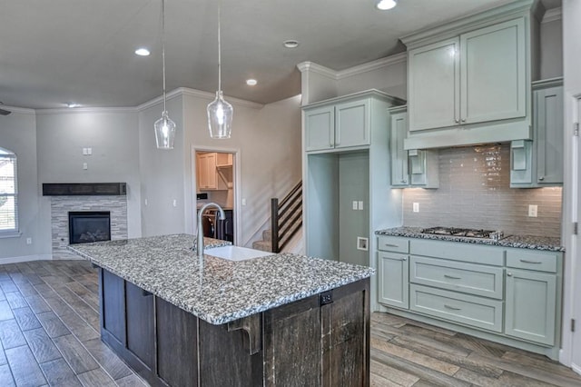 kitchen featuring dark wood-type flooring, a stone fireplace, light stone countertops, an island with sink, and decorative light fixtures