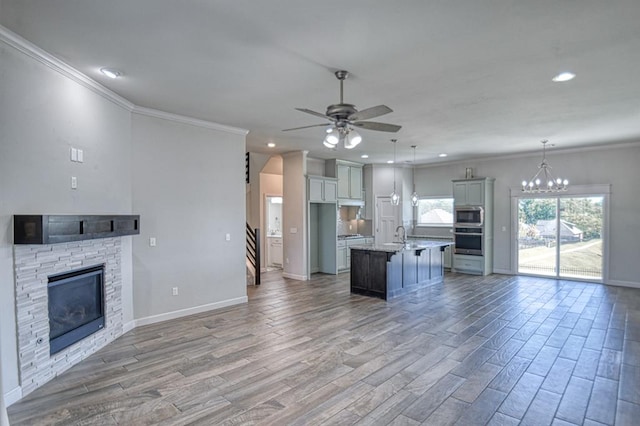 kitchen featuring a center island with sink, a stone fireplace, hanging light fixtures, ornamental molding, and wood-type flooring