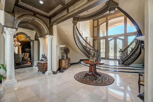 foyer featuring french doors, decorative columns, ornamental molding, light tile patterned floors, and a high ceiling